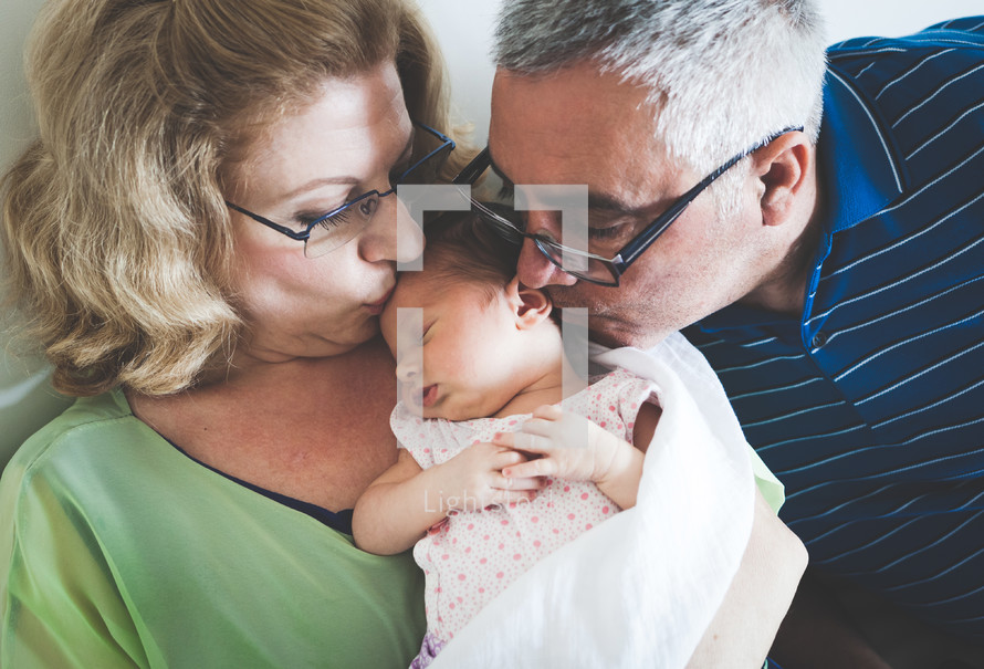 grandmother and grandfather kissing newborn granddaughter 