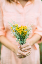 A woman in a peach dress holding a bouquet of yellow flowers.