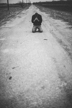 man kneeling in prayer in the middle of a rural road