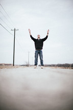 man standing in the middle of a road with his hands raised in worship to The Lord