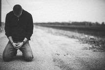 man kneeling in prayer in the middle of a rural road