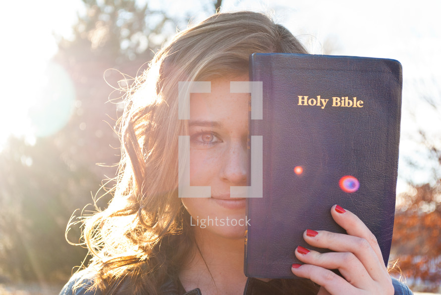 woman holding a Bible in front of half her face