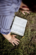 a man kneeling in grass reading a Bible 