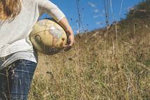 a woman standing outdoors in a field of tall grass holding a globe 