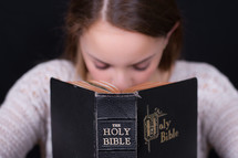 Girl praying behind a Bible.