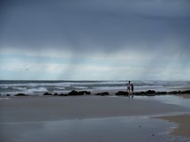 A couple of people standing on a beach along a rocky coastline at the edge of the ocean after a stormy day in Northern Florida. 