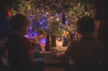 boys playing with a nativity scene under a Christmas tree 