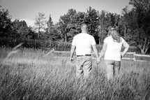 couple walking holding hands in a field of tall grasses 