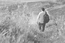 a man walking down hill carrying a Bible 