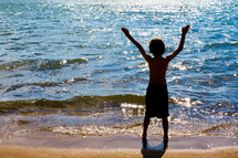 Boy with arms raised while standing at the ocean shore.
