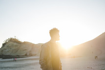 a man standing on a beach and a sunburst 