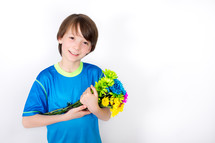 Smiling boy cradling a bouquet of flowers.