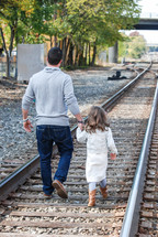 a father and daughter walking on train tracks 