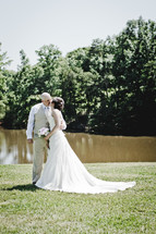 a bride in groom kissing in grass near a pond 