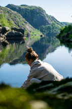 a woman sitting near a lake 
