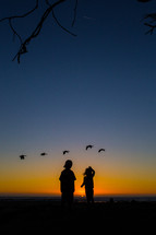 silhouettes of children watching ducks fly 