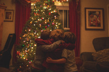 cousins hugging in front of a Christmas tree 
