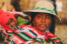 a woman in Peru carrying a baby on her back 