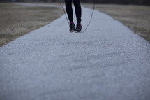 A woman jumping rope on an outdoor path.