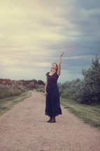 woman standing on a dirt road with hand raised praising God 