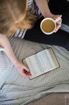 a girl sitting on a bed with coffee reading a Bible 