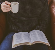 A man sitting in a chair reading the Bible with coffee