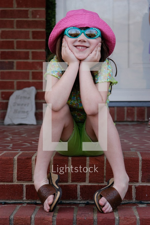 Six year old girl in sunglasses and hat posing for an informal portrait.