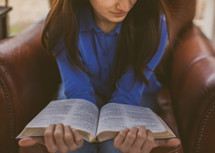 A young woman sitting in a chair reading her Bible