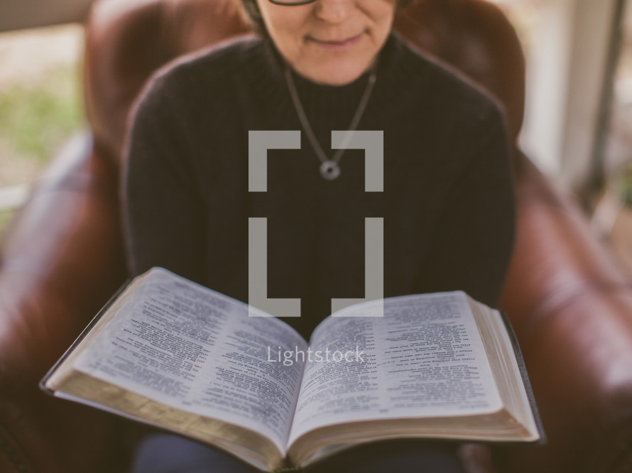 Woman reading the Bible while sitting in a chair.