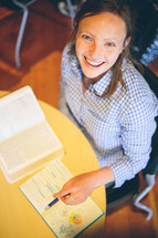 Woman sitting at a table, looking up smiling, studying her bible, making notes