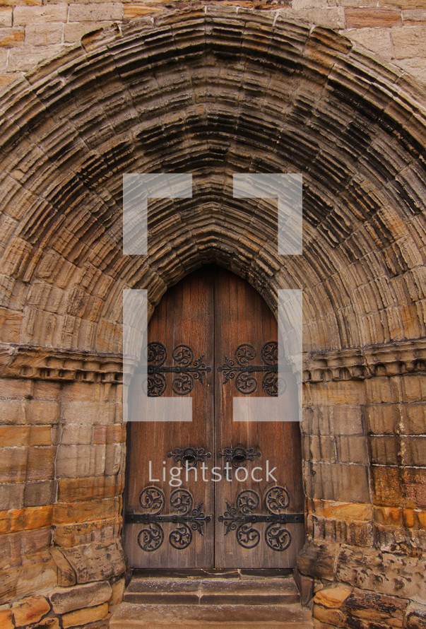 Arch over a wooden doorway of an ancient stone cathedral.