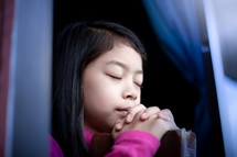 closeup of a girl child praying in an open window during quarantine 