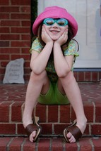 Six year old girl in sunglasses and hat posing for an informal portrait.