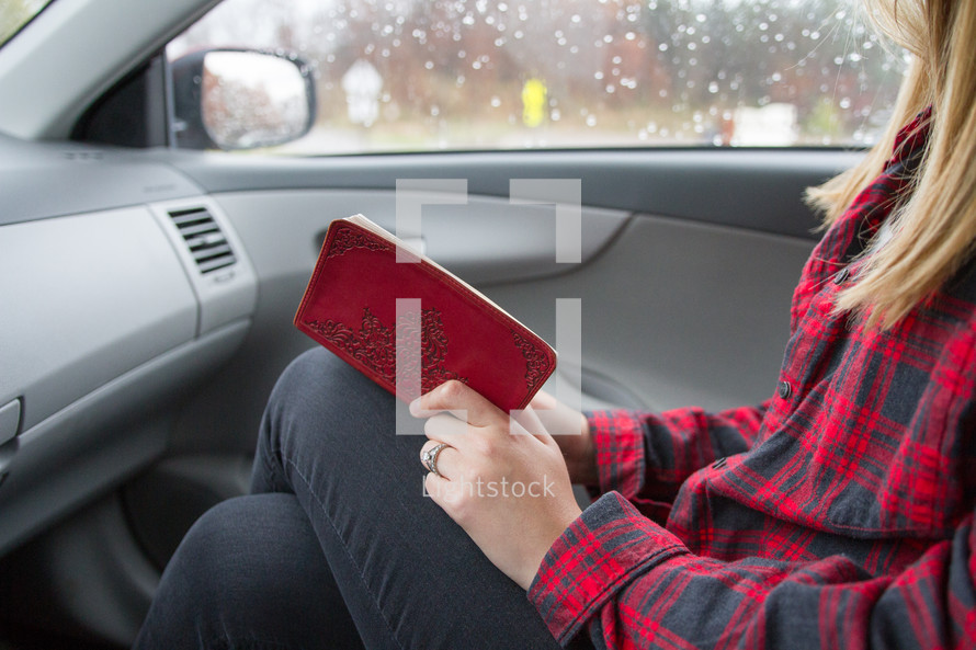 A woman sitting in the car passenger seat reading the Bible