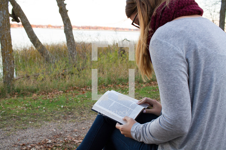 a woman sitting outdoors in fall reading a Bible 