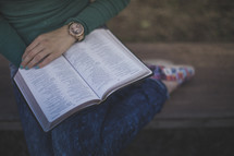 A young woman sitting on a bench reading the Bible