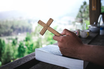 male holding a cross over a Bible praying on a balcony 