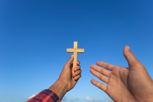 arms holding up a wooden cross towards a blue sky 
