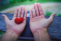 Hands with palms up on a Bible holding a red fabric heart