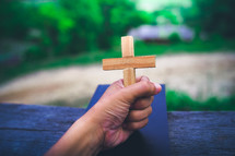 Hand holding a wooden cross on the Bible