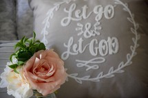 flowers and a Let Go and Let God throw pillow on a bed 