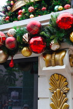 Fireplace mantle with gold and red ball ornaments and pine needles hanging from it.