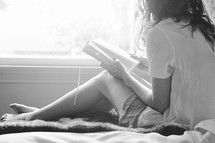 a teen girl reading a Bible on a bed 