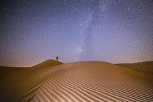 standing on sand dunes under a starry sky