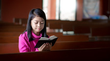 a girl reading a Bible alone in an empty church 