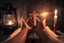 cupped hands with cross and an an open Bible with light from an oil lamp 