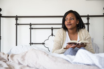 a young woman sitting in bed reading a book 