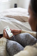 young woman sitting in bed looking at her cellphone 