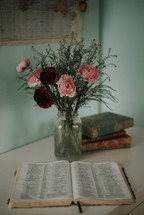 vase of red and pink flowers and an opened Bible 