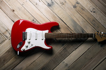 a red electric guitar on a wooden table.